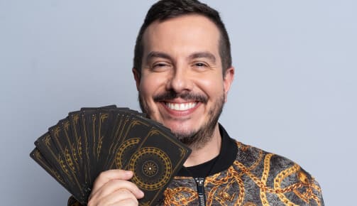 Foto do André Mantovanni sorrindo segurando as cartas de tarô em leque