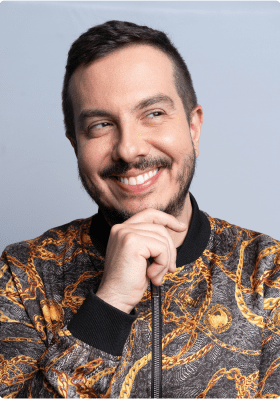 Foto do André Mantovanni sorrindo com a mão apoiada no queixo