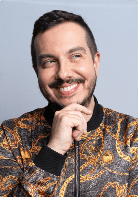 Foto do André Mantovanni sorrindo com a mão apoiada no queixo Foto do André Mantovanni sorrindo com a mão apoiada no queixo
