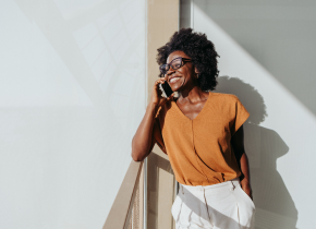 mulher negra usando óculos com uma blusa marrom falando ao telefone e sorrindo