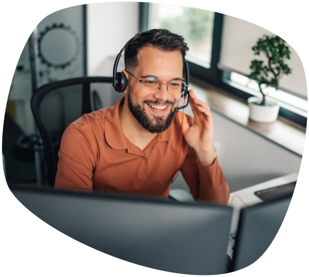 homem branco com barba usando óculos e headphones em frente ao computador